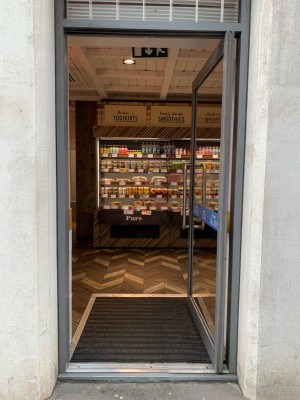 Glass door with grey frame ahead. Push from handle on left to open.