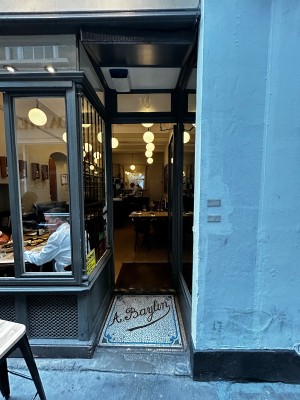 Single glass door with black frame. Golden handle on left. Push to open. Path narrows before door.