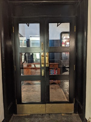 Glass and wood door with black frame and metal handles in centre. Pull to open.