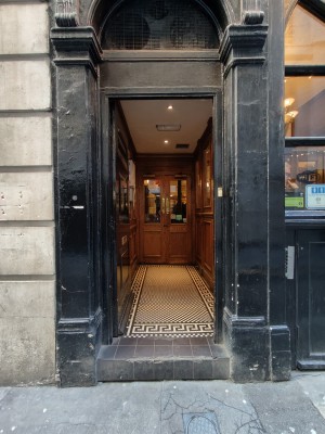 Facing black framed glass door. Push golden metal handle on right to open. Doorbell for assistance on right.