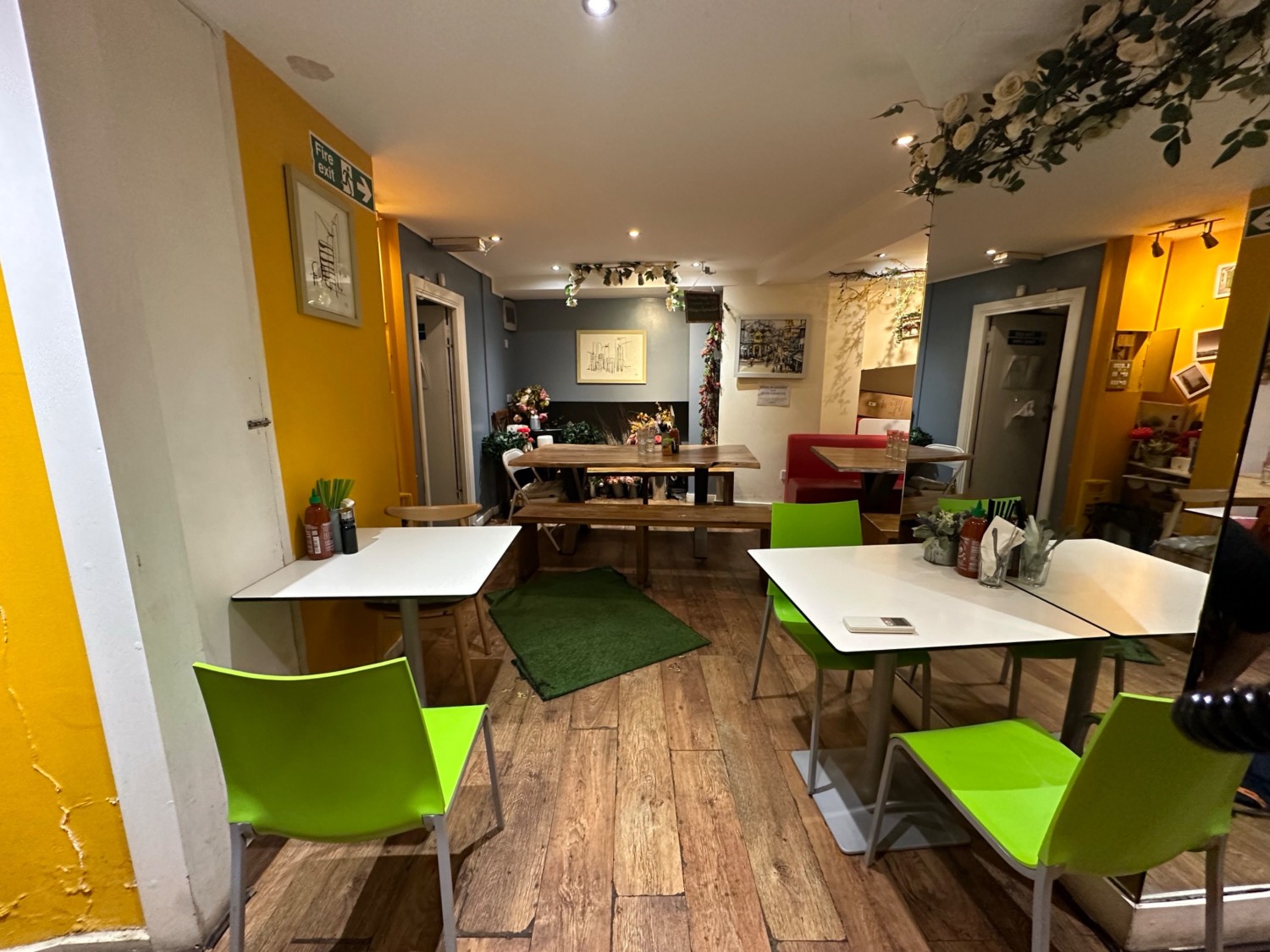 From bottom of stairs looking straight at path ahead. Toilet to left. Tables and chairs to far left and right. Table with benches on back wall ahead.