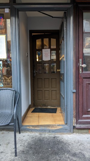 Grey wooden preceding door with glass paneling. Push from handle on left to open.