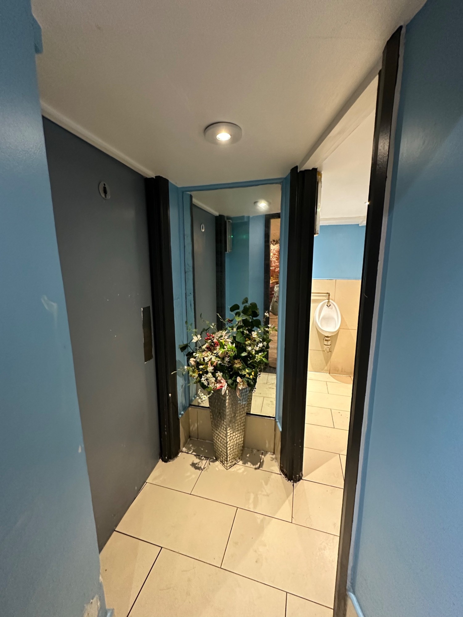 From door looking straight at preceding door on left to women’s bathroom. Preceding door on right to men’s bathroom.