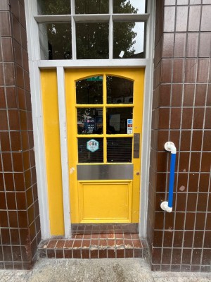 Yellow door with glass panels. Push from right to open. Grab rail to the right of door.