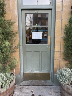 Glass door with grey frames. Push brass pad on right to open.
