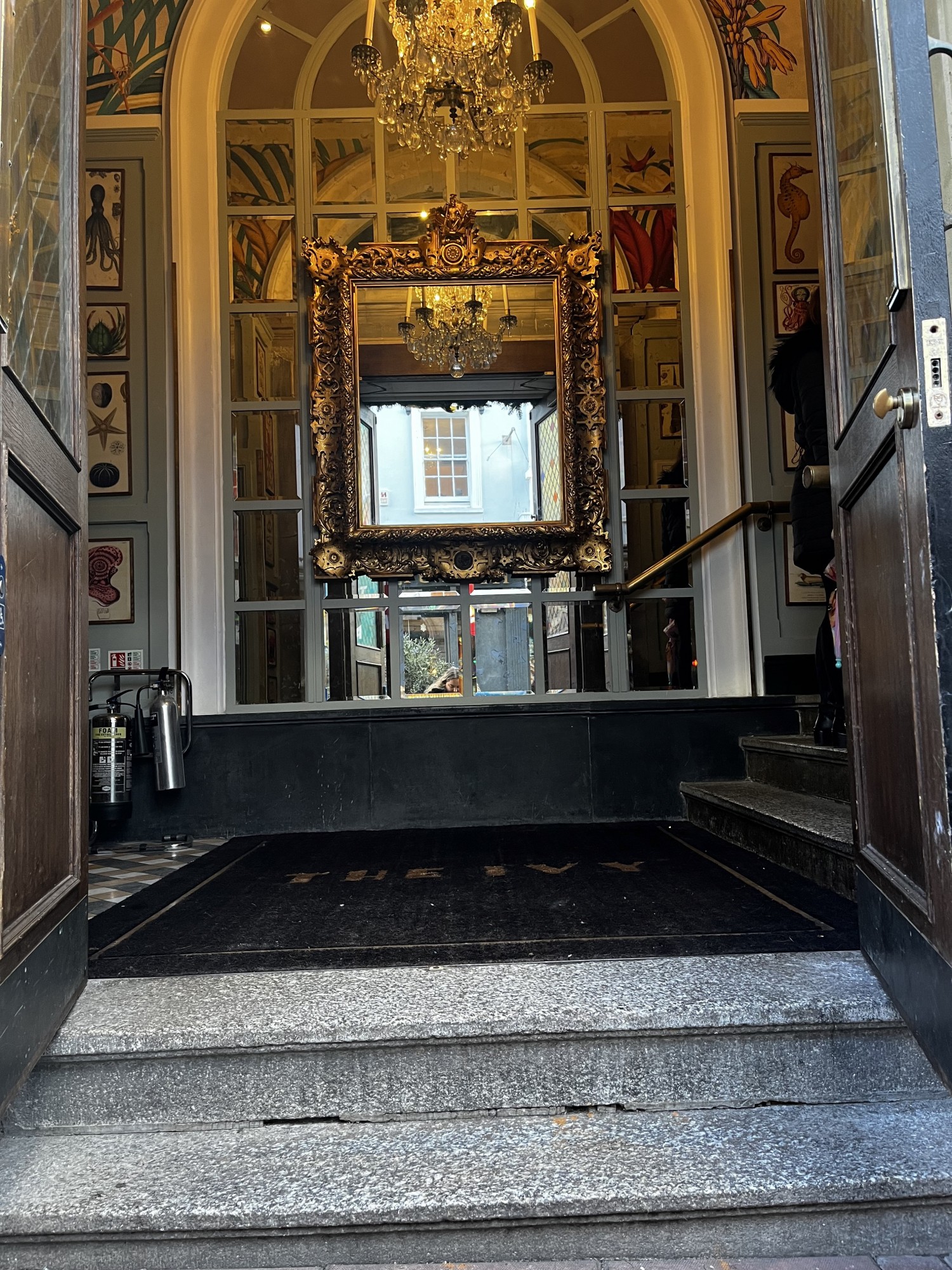 Photo shows wide double door way up steps and once inside on the right further steps. Large mirrors straight ahead. Entrance to restaurant and waiting to be seated is up second set of steps. Doors open inwards.