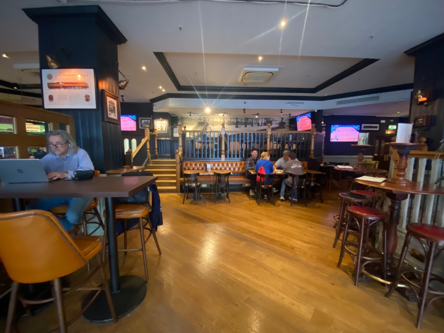 From mid-path in front of entrance, facing straight. High tables and stools on both sides. Half booth, tables and chairs along back wall.