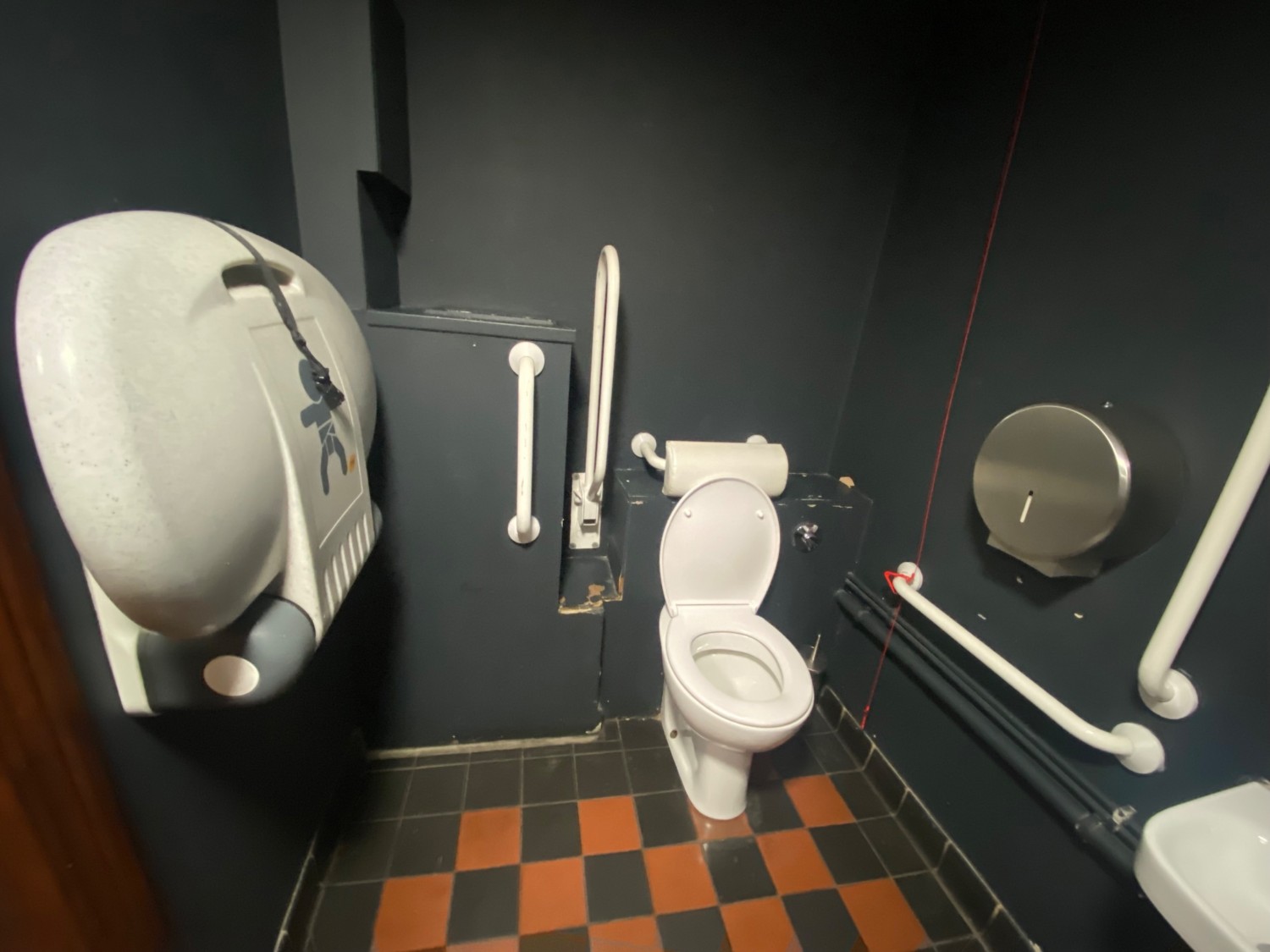 From door, facing left. Toilet on right. Emergency pull cord on its right. Baby change on left.