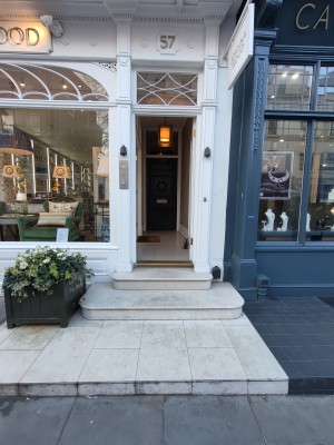 Three steps up to white framed glass preceding door. Push from left to open. Doorbell for assistance on left of door.