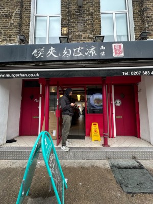 From pavement looking straight at covered entrance ahead with red pillars to left and right before entrance. A-frame and small step before entrance.