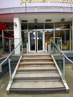 From sidewalk facing venue. Path to entrance in front. Staircase going up. Handrails along both sides.