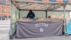 From street looking straight at market stall. Standard height stall under a canopy with food displayed on top and server behind.