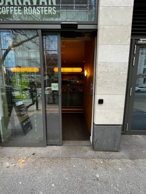 Automatic sliding glass door with black doorframe. Slide to the left to open.