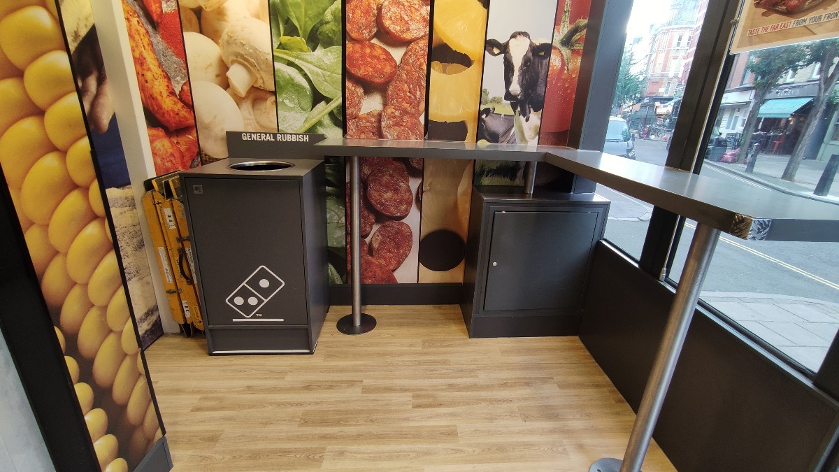 From door facing right. Path ahead. High table along right and back walls. Bin at back left.