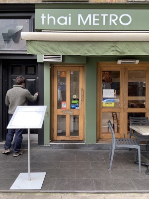 Single glass door with light wooden frame and vertical silver metal handle along right. Pull to open.