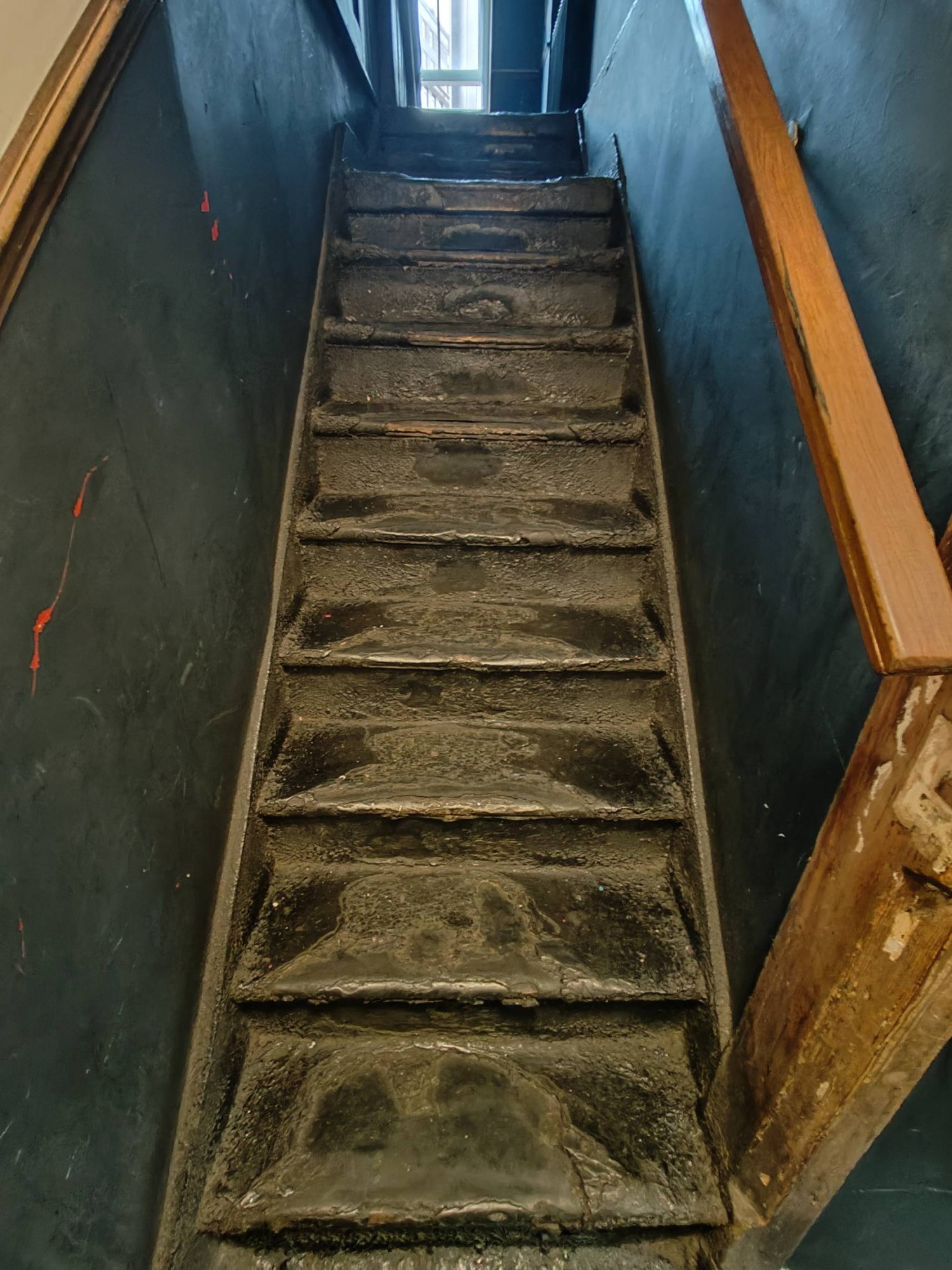 From top of stairs facing right. Stairs going up to upstairs area. Hand rail on right.