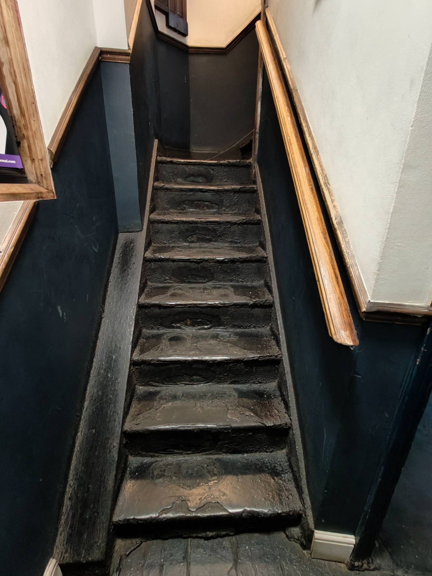 From door facing right then right. Stairs going up to upstairs area. Hand rail on right.