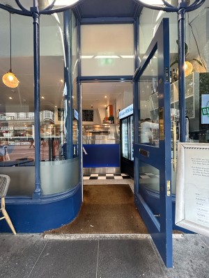 Glass door with bright blue wooden frame ahead. Vertical gold metal handle on left, pull to open.
