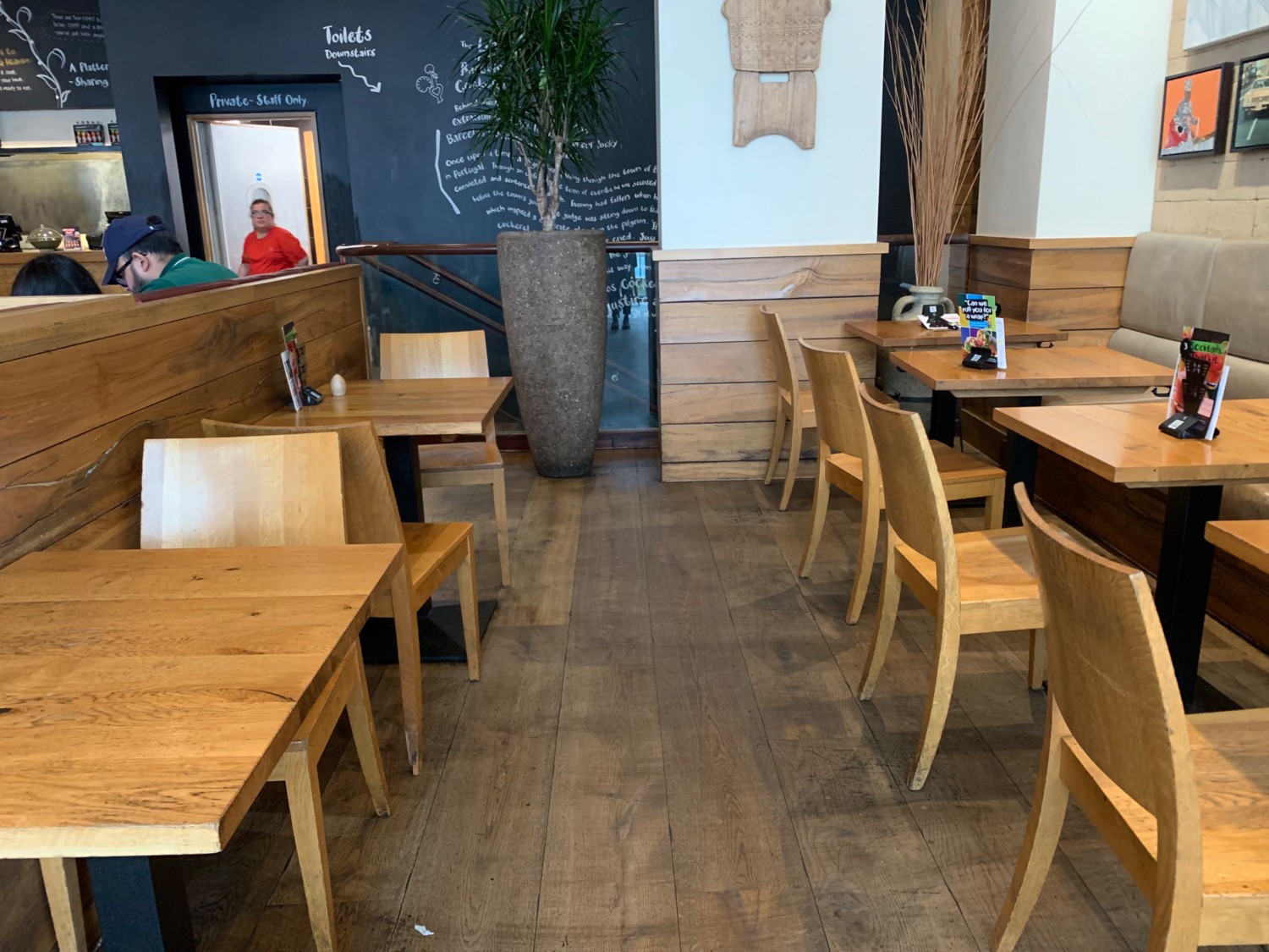 From end of right path, looking left. Tables and chairs along left wall divider. Path down center. Half booths along right wall.
