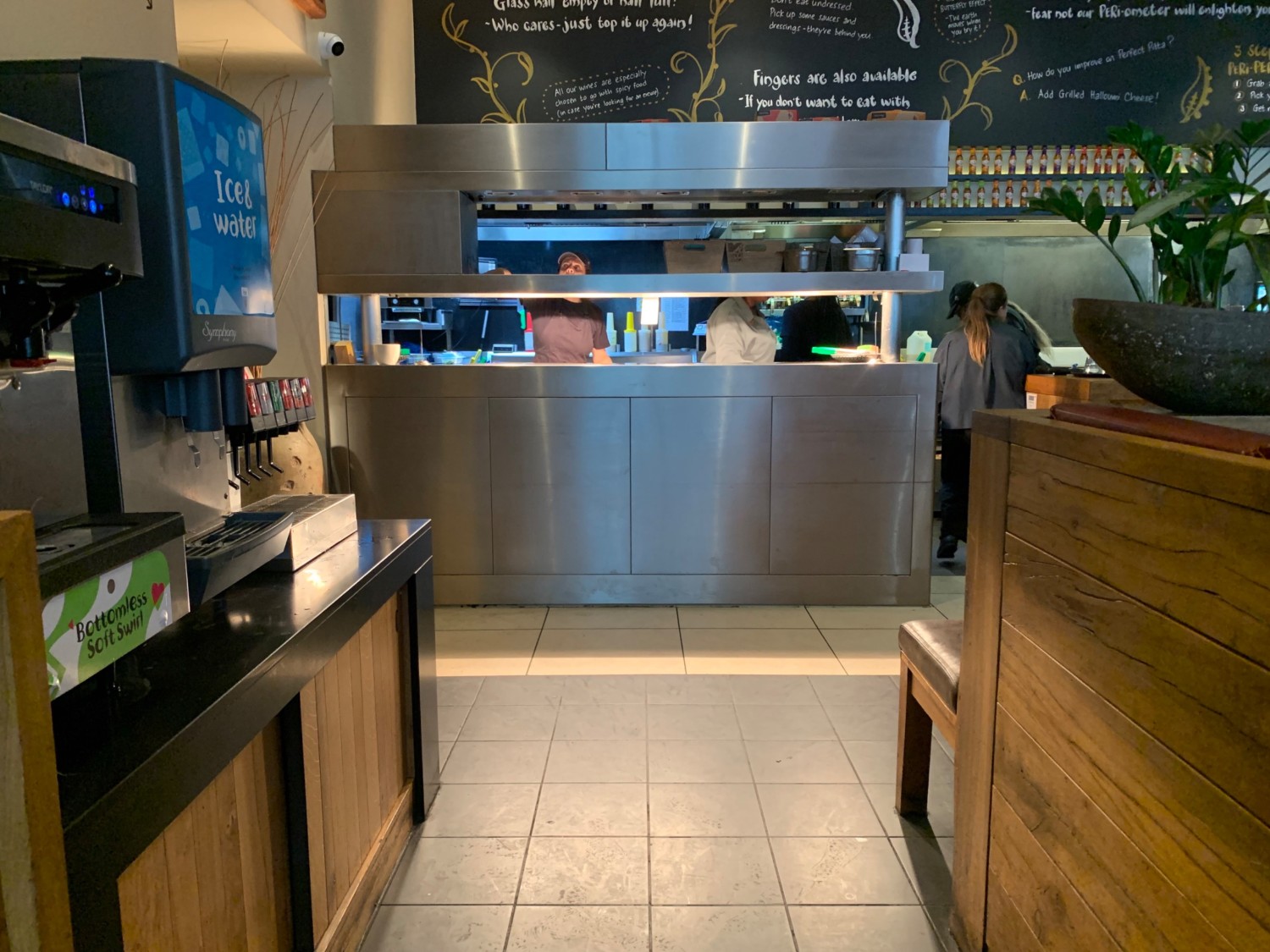 From end of path, looking right. Wall divider on right. Path straight to kitchen ahead and toilet area to back of left wall. Staff counter on left.