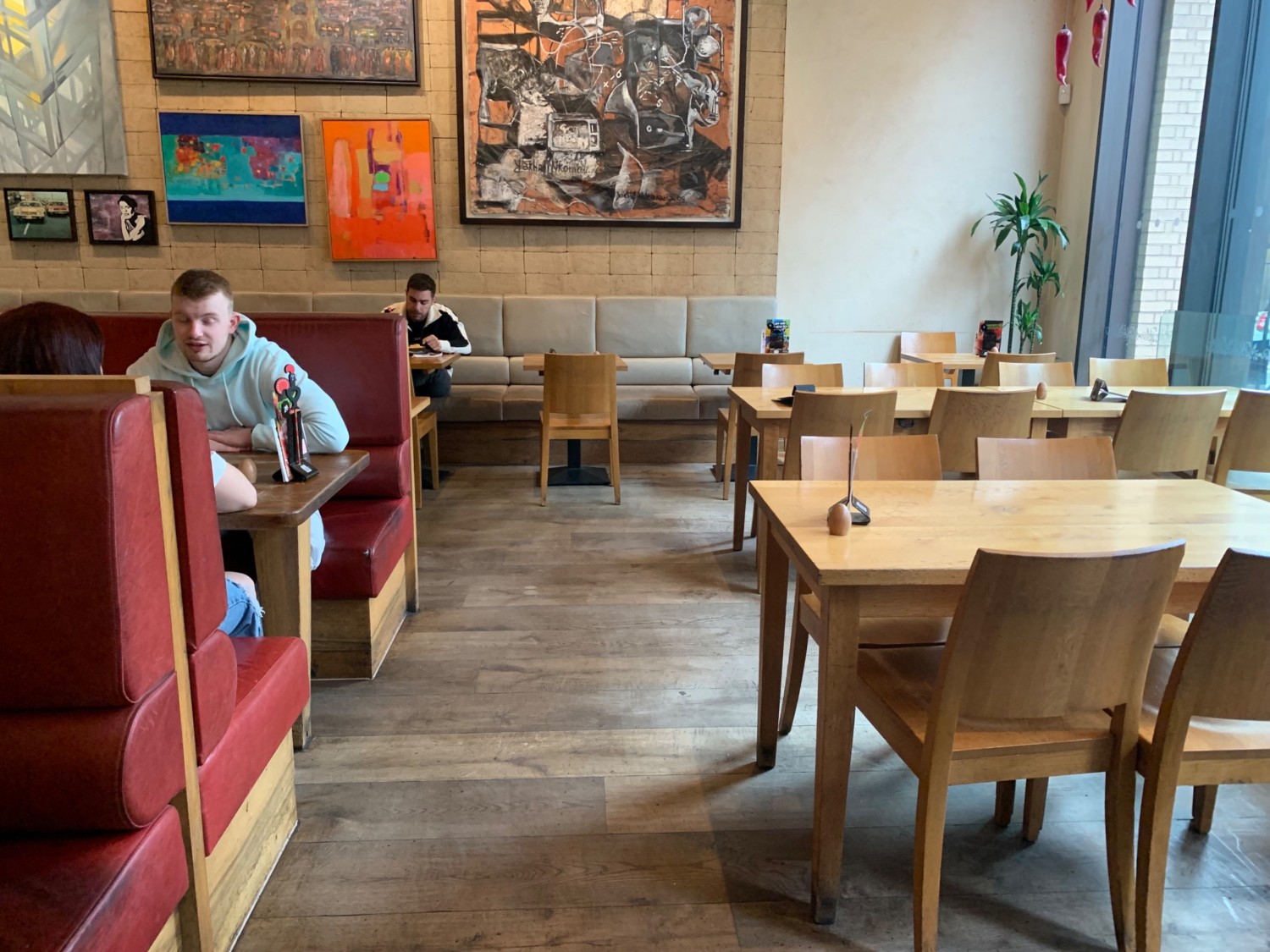 From entrance, looking right. Tables and chairs along right wall. Path straight to half booths along back wall. Booths along left wall divider.