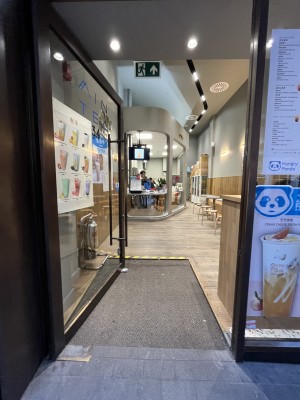 Glass door with black frames ahead. Push to right via vertical metal handle to open.