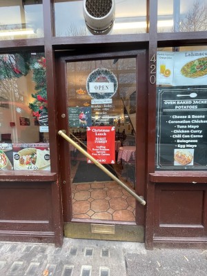 From sidewalk facing venue. Glass entrance door with brown frame. Push to open metal handle in center.
