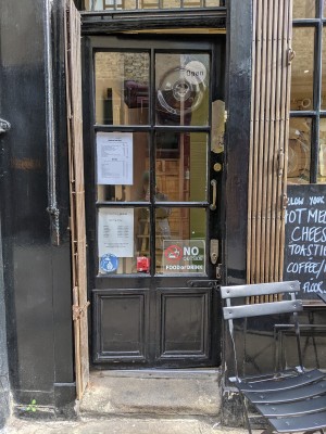 Glass door with black frame and metal handle on right. Push to open.