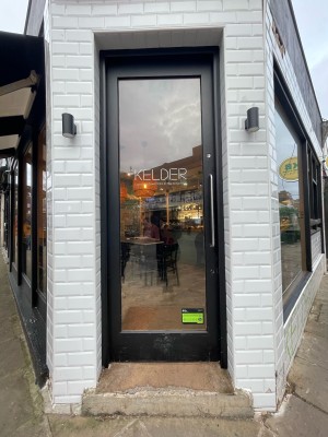 From sidewalk facing venue. Glass door with black frame. Push to open metal handle on right.