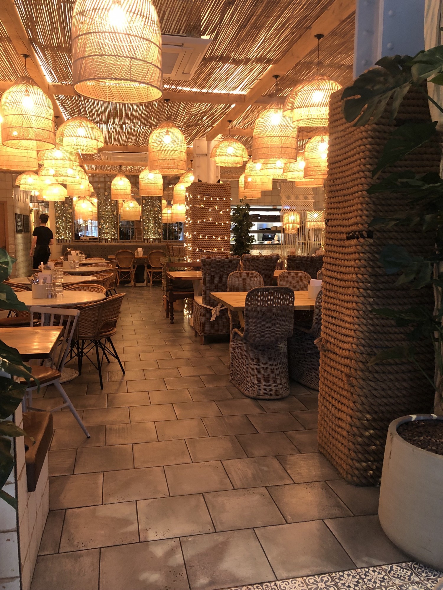 View from the entrance. Straight ahead from the entrance it is located the side area. Straight ahead there is a pathway and at the end next to the wall a bench with seating height tables.