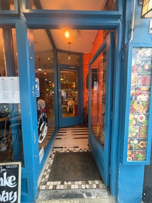 From back left of outdoor area facing left. Glass door with blue frame ahead. Push at center left to open.