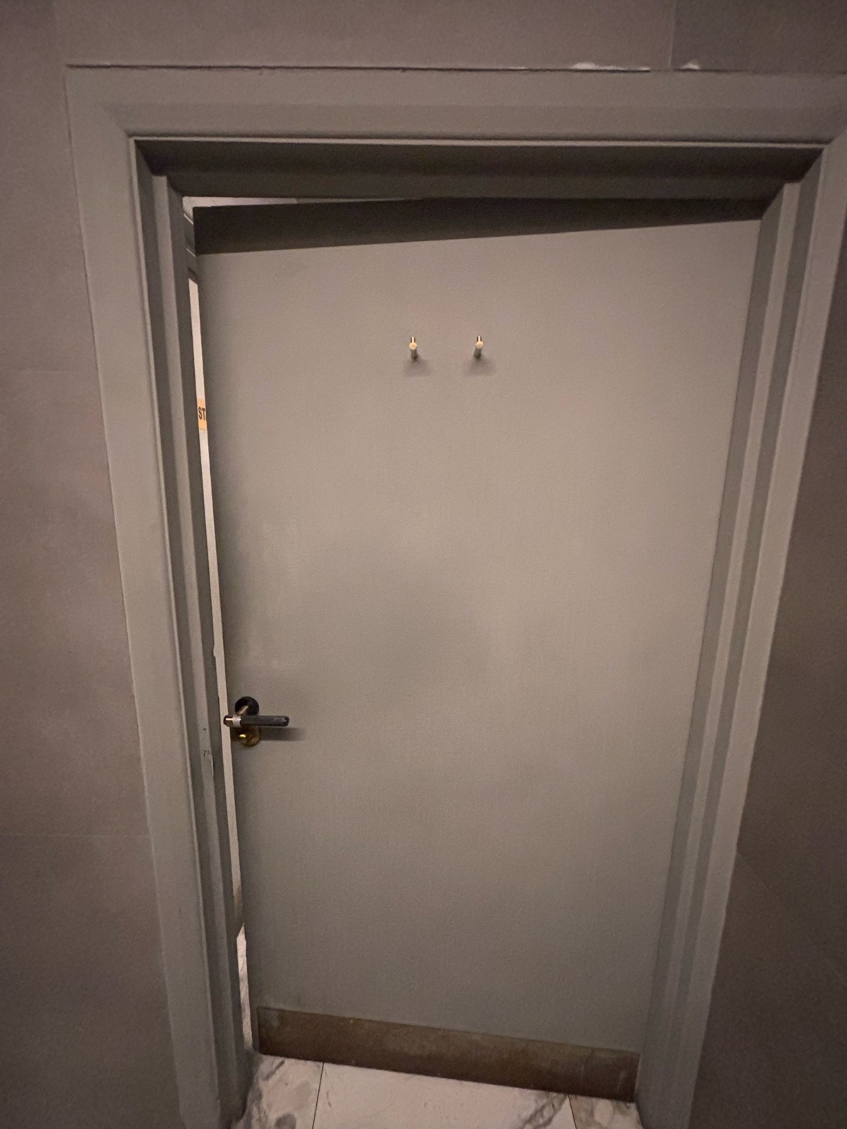 Back of bathroom door. Hanging hooks at center top of door. Push metal handle at center left to open.