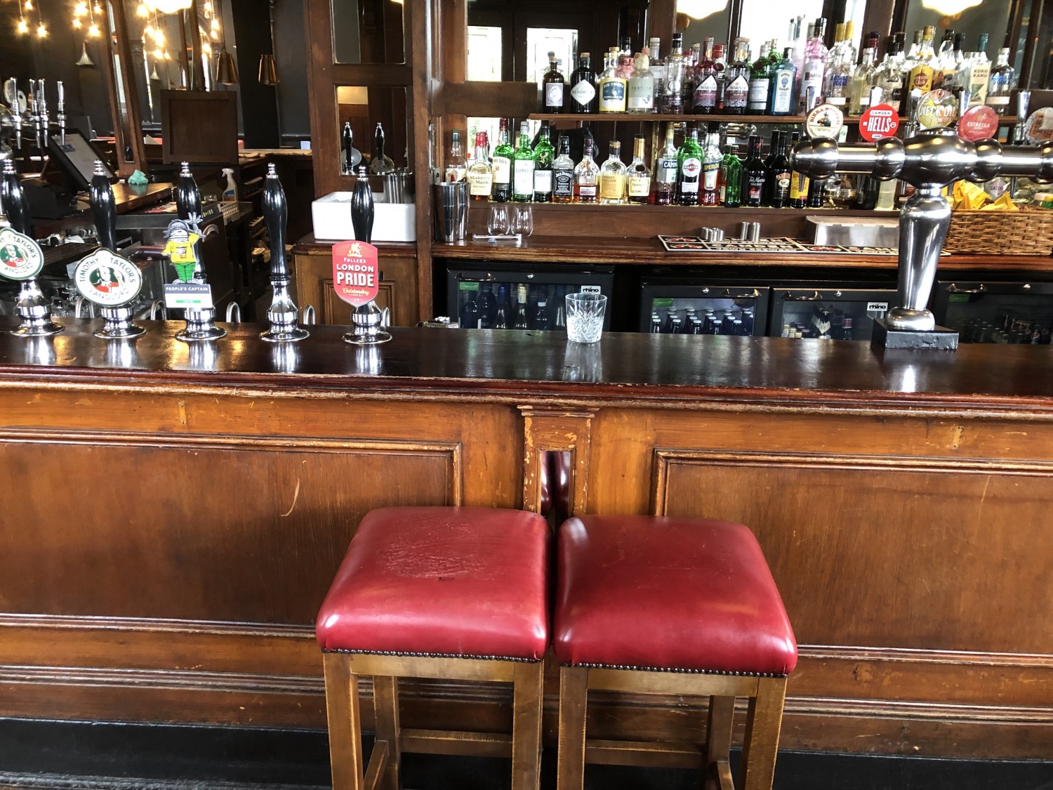 Photo from main entrance looking ahead. Bar is straight ahead and goes around to the left and right. Pictured are two stools in front of the bar.