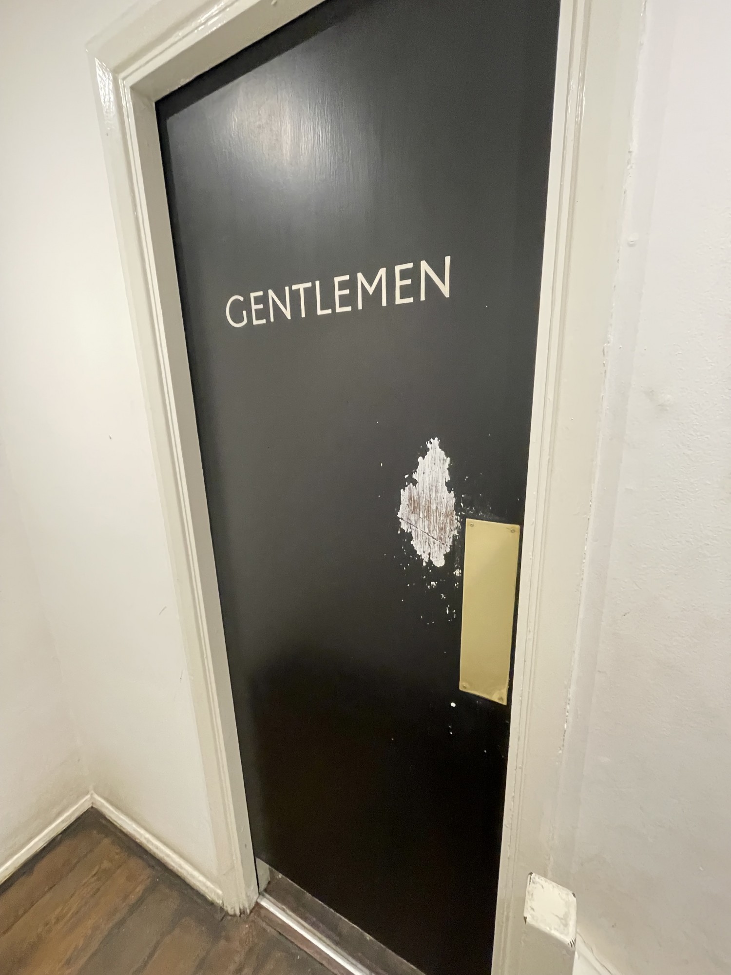 Preceding door to cubicles in gents bathroom. It is a push door. Should be pushed from the right. Found at the top of stair case to the right.