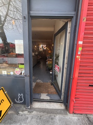 Glass door with dark grey frame ahead. Push metal handle on left to open.