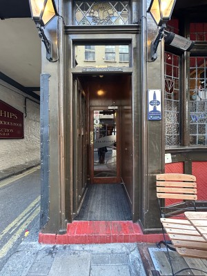 Preceding dark brown single wooden door with gold pad on right, push to open. Step at foot of door.
