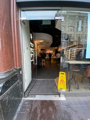 Glass door, silver handle on right. Push to open. Assistance button to left of door.