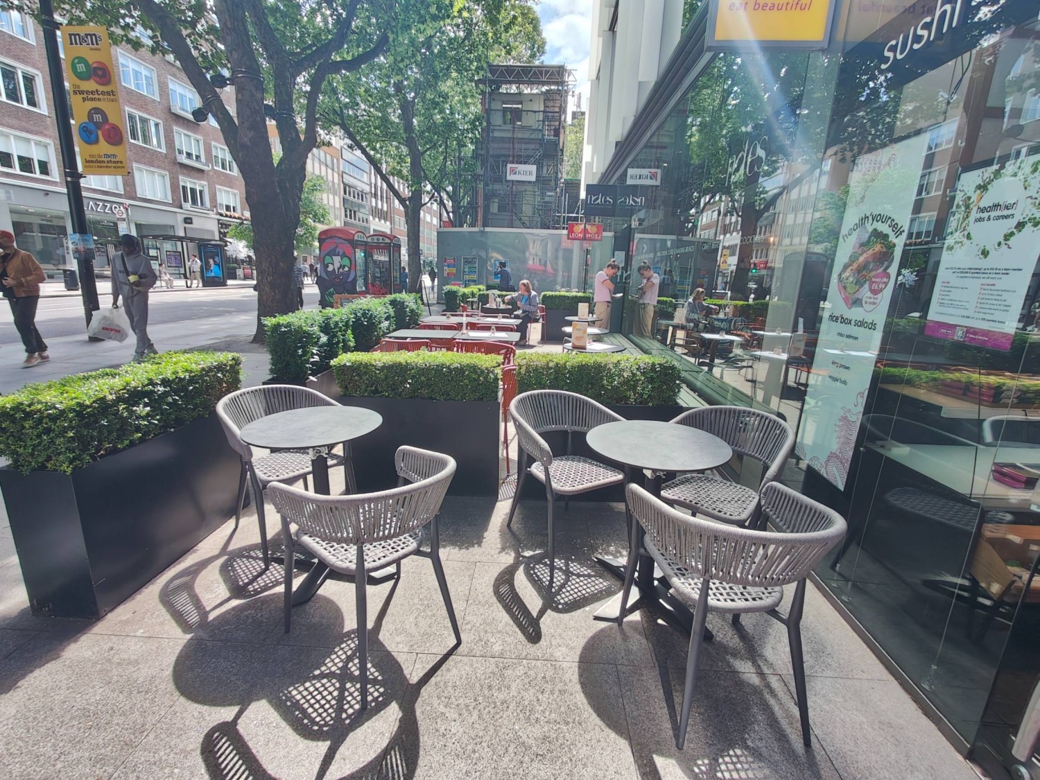 From entrance path facing left. Tables and chairs along back. Plants fence on left and back.