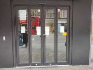 Picture of main entrance. It is an automatic double door that folds completely open from the middle to the right and the left. There is a small bump when entering.