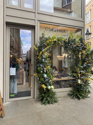 Front entrance of Chestnut Bakery Convent Garden. Door on left hand side  with door handle on right side of the door. Flower decoration all over the wall on right hand side of the door.