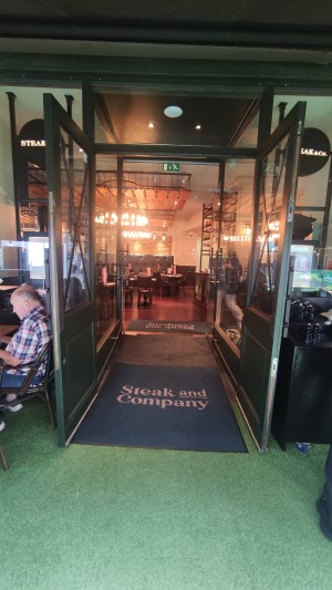 Two sets of pull manual doors ahead. First set made of glass with green wooden frames. Vertical pull handle in centre.