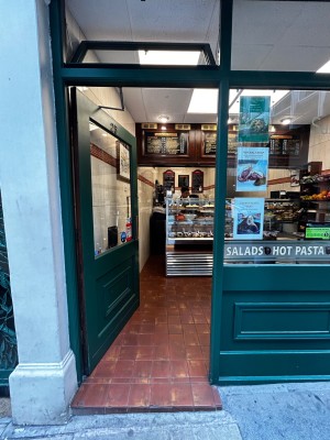 Facing single green glass door with golden handle on the right. Push to open.