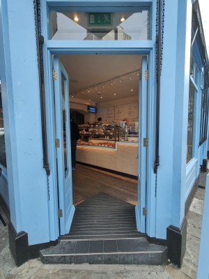 Facing blue framed double glass doors. Push from centre to open.
