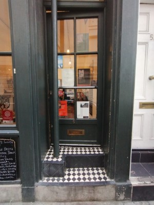 Picture of main entrance. There are two large steep steps. You have to push the door open to the right. The handle is on the door in the middle. At the left is a pole.