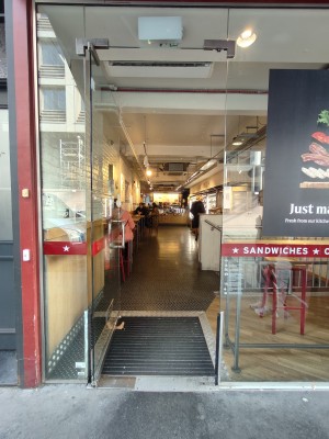 Facing single glass door. Push silver handle on right to open.
