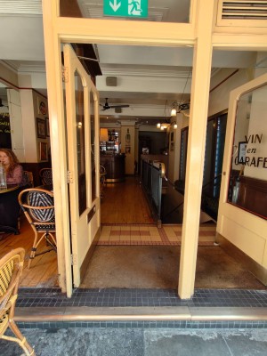 Facing white framed entrance door. Push silver metal panel on right of door to open.