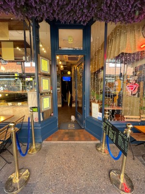 Single glass door with blue frame. Push golden vertical handle on left to open. Rope fence to left and right of entrance.