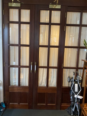 View of storage room door located on left hand side as you enter the door. Available for crutches and any other accessibility tools that require storage. Double door with door handles in the middle. On the right is a pram folded up.