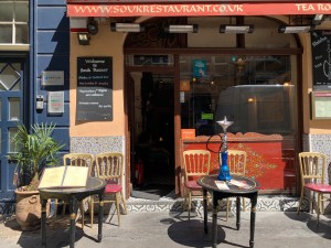 From street, facing entrance. Path straight to entrance door ahead. Outdoor seating to left and right of entrance door.