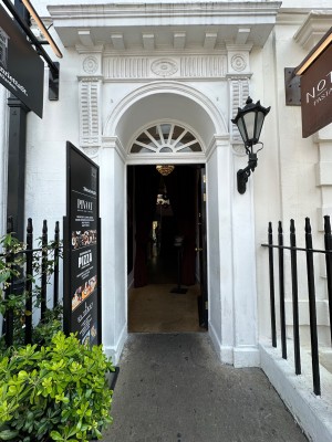 From pavement looking at path ahead. Black fences to left and right. Black door with gold handle to left of door, push to open.